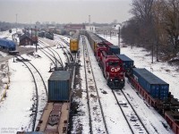 A pair of SD40-2's CP 5645 and CP 5656 with a train of autoracks are facing east in this view of CP's Quebec Street Yard in London, taken from Quebec Street overpass.  The adjacent container train is single-stacked, otherwise it could not pass through the Detroit-Windsor tunnel. <br><br>Over to the left under blue covers are two new Irish Rail (Iarnród Éireann) JT42HCW locomotives, units 232 and 230 on flatcars.  Ireland's wide rail gauge of 5' 3" prevents them travelling on their own wheels to their ship; their 3-axle trucks travel on another flatcar. <br><br>Behind the pole to the right of tarped unit 232, the front of a locomotive coloured pale green can be seen. In this timeframe it is probably a new SD60i for Conrail, presumably in transit to them in primer.<br><br>Unfortunately the view west from this bridge is obstructed by cables that cross the tracks here.